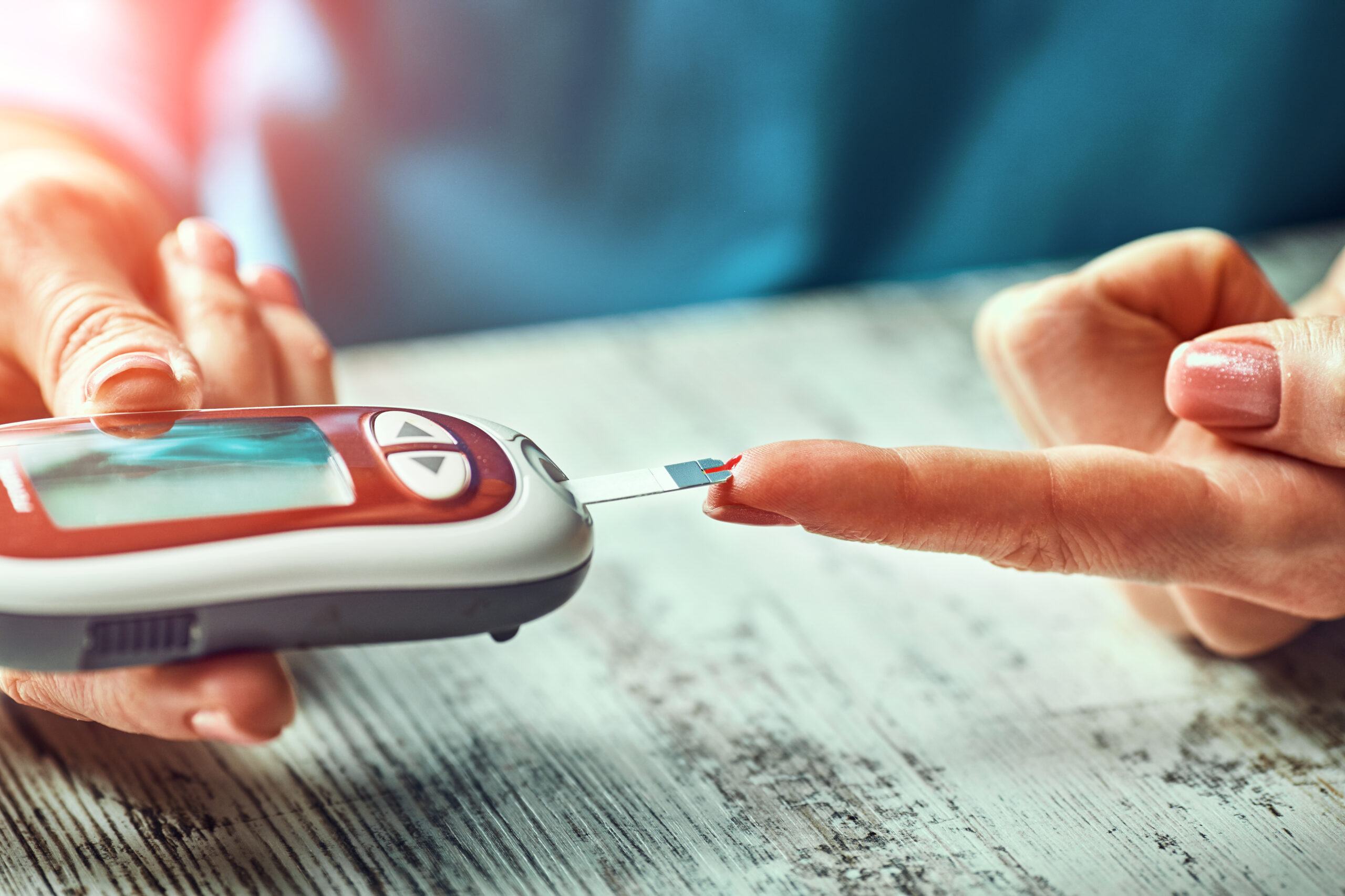 A close-up image showing a person’s hand using a glucometer to check their blood glucose level. The individual is pricking their finger with a lancet to draw a small drop of blood for the test.